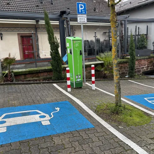 Eine Ladesäule für Elektroautos steht auf einem Parkplatz. Neben der Säule sind markierte Stellplätze für Elektrofahrzeuge zu sehen.