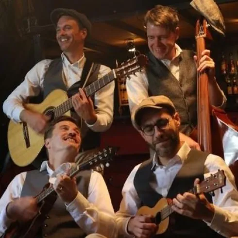 Eine Band spielt Musik auf verschiedenen Instrumenten. Die Musiker tragen klassische Anzüge und haben viel Spaß beim Auftritt.