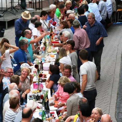Eine große Gruppe von Menschen sitzt an einem langen Tisch und genießt ein gemeinsames Essen. Die Atmosphäre sieht freundlich und festlich aus.