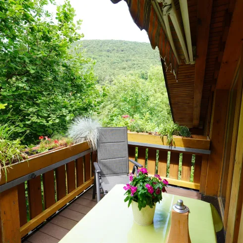 Ein gemütlicher Balkon mit einem Tisch und einem Stuhl. Umgeben von üppigem Grün und einer schönen Aussicht auf die Natur.