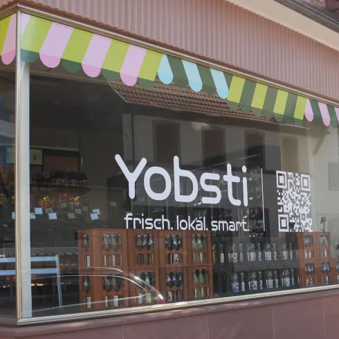 Ein Schaufenster eines Geschäfts mit dem Namen "Yobsti". Die Fensterfront zeigt bunte Dekorationen und einen QR-Code.
