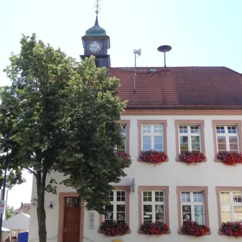 Ein hübsches Gebäude mit einer Uhr und bunten Blumenkästen. Vor dem Haus steht ein großer Baum.