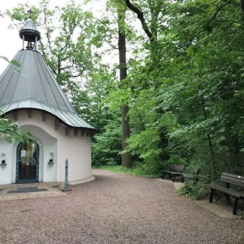 Ein kleiner Pavillon umgeben von Bäumen in einem ruhigen Park. Auf der gegenüberliegenden Seite sind zwei Bänke zum Entspannen.