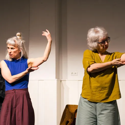 Zwei Frauen führen eine künstlerische Bewegung darstellende Performance auf. Sie stehen in einem hellen Raum und zeigen mit ihren Armen verschiedene Posen.
