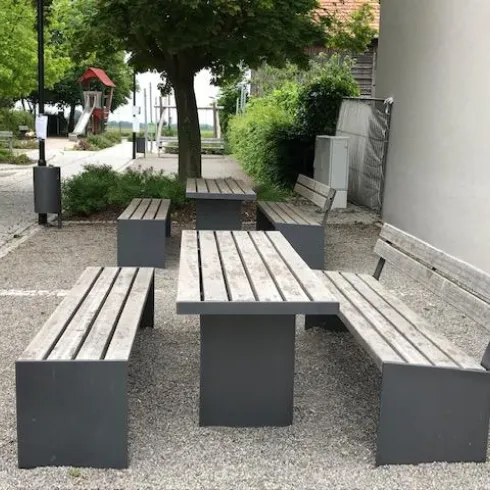 Ein moderner Tisch mit Bänken im Freien, umgeben von grünen Bäumen. Der Bereich ist sauber und gut gestaltet, ideal für entspannte Treffen.