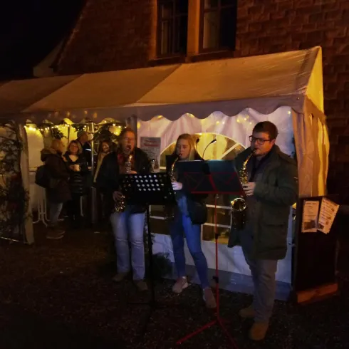 Eine Weihnachtsveranstaltung mit Musikern, die Saxophon spielen. Im Hintergrund ist ein beleuchteter Festzelt und Zuschauer sind zu sehen.
