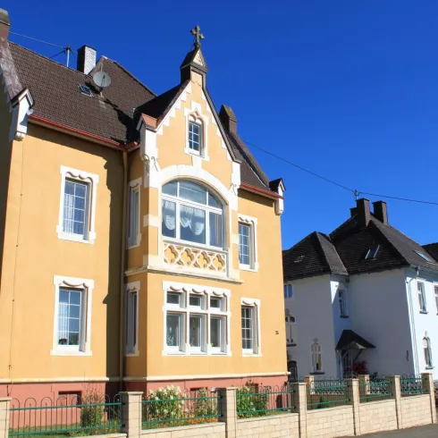 Ein farbenfrohes, historisches Wohnhaus mit einem schönen Erkerfenster. Im Hintergrund steht ein weiteres Gebäude im traditionellen Stil.