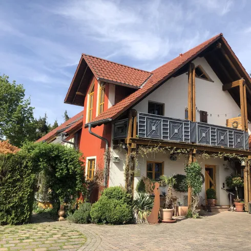 Ein charmantes Haus mit roter und weißer Fassade. Der Balkon und die grünen Pflanzen verleihen der Umgebung eine einladende Atmosphäre.