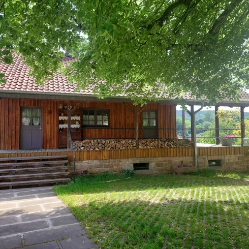 Ein charmantes Holzhaus mit rotem Dach und einer gemütlichen Veranda. Vor dem Haus liegt ein gepflegter Garten mit viel Grün.