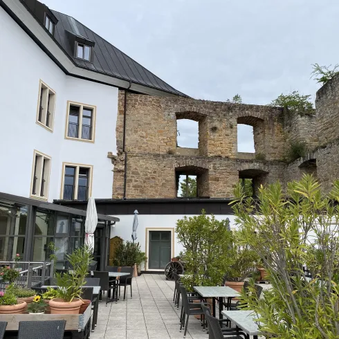Eine Mischung aus alten Ruinen und modernem Gebäude. Der Bereich ist mit Tischen, Pflanzen und einer Terrasse gestaltet.
