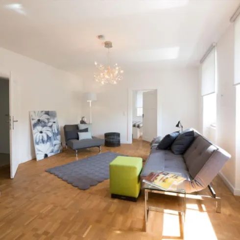 Ein helles Wohnzimmer mit modernen Möbeln und einem schönen Holzboden. Der Raum hat große Fenster, die viel Licht hereinlassen.