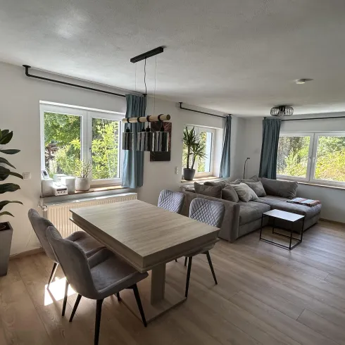 Ein helle und moderne Wohnküche mit einem Esstisch und gemütlicher Couch. Große Fenster lassen viel Licht herein und schaffen eine freundliche Atmosphäre.