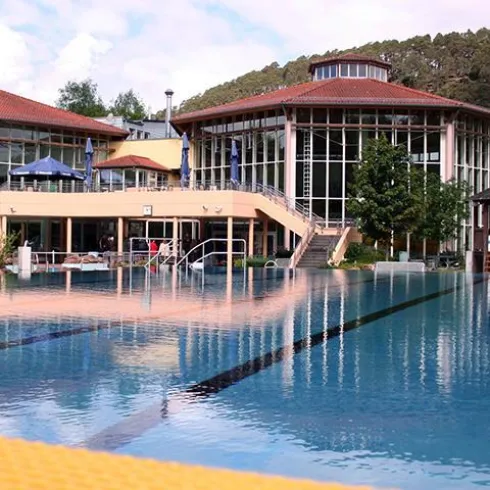 Ein modernes Schwimmbad mit klarem Wasser und einer gut gestalteten Umgebung. Im Hintergrund befindet sich ein elegantes Gebäude umgeben von Bäumen.