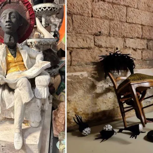 Eine stilisierte Statue einer sitzenden Person mit einem sonnigen Hut und bunter Kleidung. Daneben liegen unheimliche, kreative Objekte auf dem Boden, inklusive einer umgedrehten Stuhl.