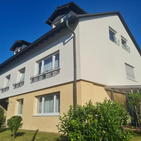 Ein modernes Haus mit zwei Etagen und einem gepflegten Garten. Der Himmel ist klar und blau.