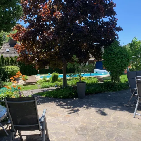 Ein wunderschöner Garten mit einem Swimmingpool und grünem Pflanzen. Ein Tisch mit Stühlen lädt zum Entspannen ein.