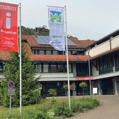 Ein modernes Gebäude mit mehreren Flaggen im Vordergrund. Die Umgebung ist grün und einladend, ideal für Touristeninformationen.