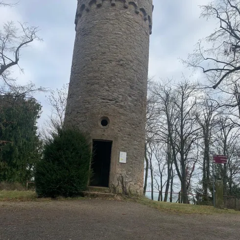 Ein steinerner Turm umgeben von kahlen Bäumen. Der Himmel ist bewölkt und die Umgebung ist ruhig.