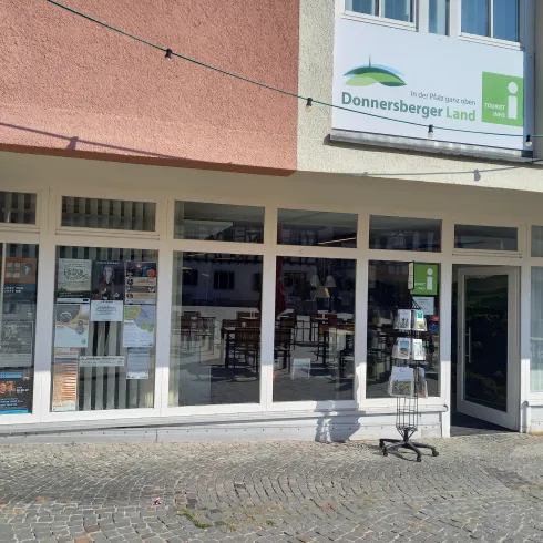 Ein Geschäft mit großen Fenstern, die zahlreiche Plakate und Informationen anzeigen. Über dem Eingang befindet sich ein Schild mit der Aufschrift "Donnersberger Land".