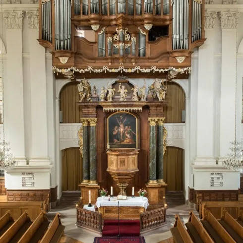 Eine prächtige Kirche mit einer großen Orgel im Hintergrund. Der Altar ist im Mittelpunkt, umgeben von Holzbänken und einem Teppich.