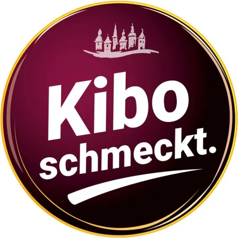 Ein runder, lila Logo mit dem Text "Kibo schmeckt." in großen, weißen Buchstaben. Darüber ist eine Abbildung von Gebäuden zu sehen.