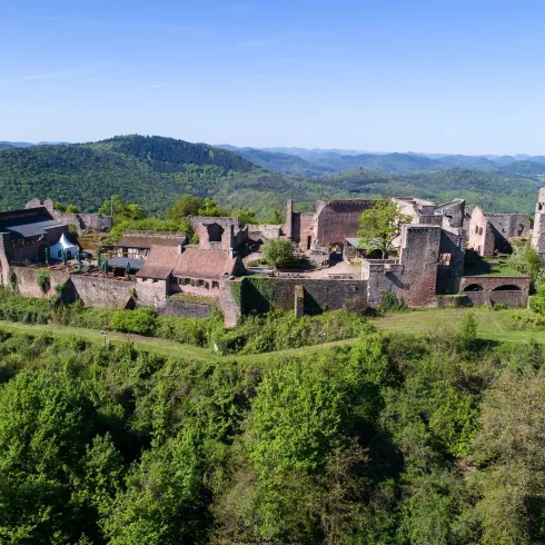 Eine beeindruckende Burgruine umgeben von grünen Hügeln. Der blaue Himmel und die Natur verleihen der Szenerie eine malerische Atmosphäre.