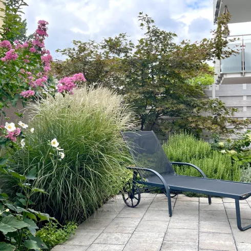 Ein schöner Garten mit bunten Blumen und grünen Pflanzen. Eine Liege lädt zum Entspannen ein.