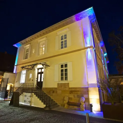 Ein charmantes Gebäude bei Nacht, beleuchtet mit bunten Lichtern. Die Fassade ist gut sichtbar, und es gibt eine einladende Treppe.