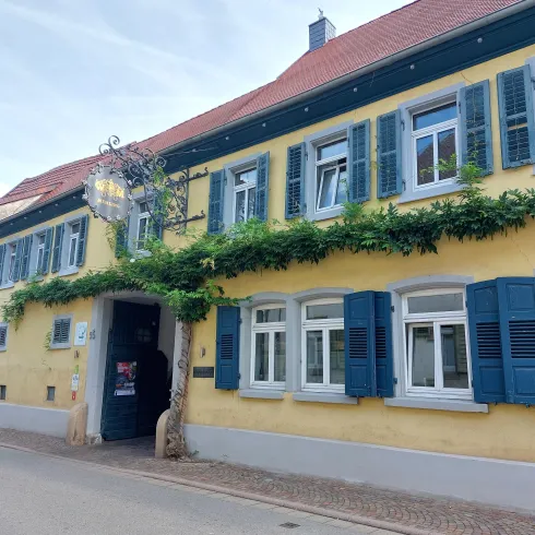 Ein charmantes gelbes Gebäude mit blauen Fensterläden. Grünes Efeu rankt an der Fassade.