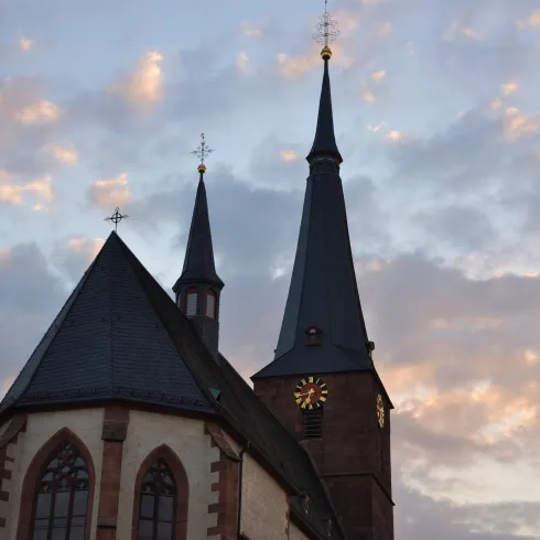 Eine Kirche mit hohen Türmen und einem historischen Stil. Der Himmel ist mit sanften Wolken in verschiedenen Farben geschmückt.