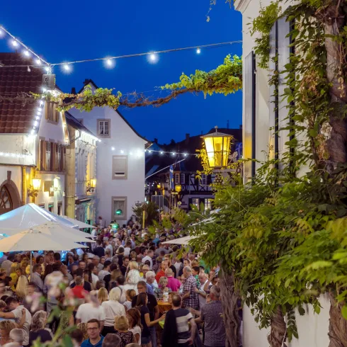 Fröhliche Menschen feiern auf einem Platz unter nächtlichem Himmel Weinfest in Deidesheim.
