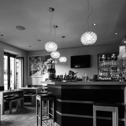 Ein stilvolles Café mit Holzstühlen und einer modernen Bar. Die Wände sind mit Kunstwerken dekoriert und es gibt große Fenster, die für gutes Licht sorgen.