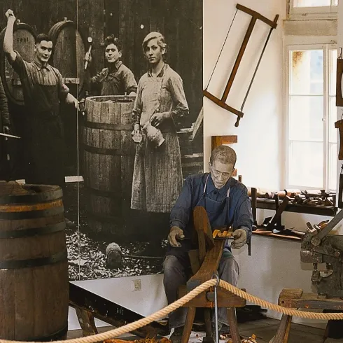 Eine historische Werkstatt mit Holzfiguren und Werkzeugen. Im Hintergrund ist ein großes Schwarz-Weiß-Bild von Arbeitern zu sehen.