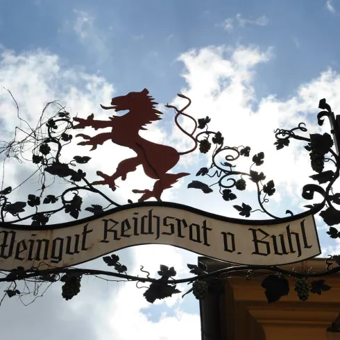 Ein dekoratives Schild des Weinguts Reichsrat von Buhl. Im Hintergrund sind Wolken am Himmel sichtbar.