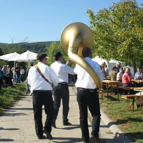 Fröhliche Menschen sitzen an Bierzeltgarnituren mitten in den Deidesheimer Weinbergen. Vor ihnen spielt eine Jazzband.