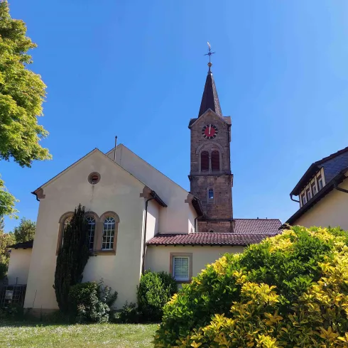 Eine charmante Kirche mit einem hohen Turm und einer Uhr. Umgeben von grünem Gras und Bäumen im strahlenden blauen Himmel.
