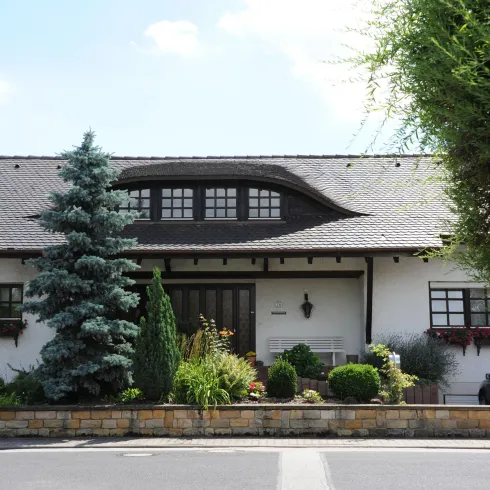 Ein charmantes Haus mit einem grauen Dach und weißen Wänden. Der Garten ist schön gepflegt und mit verschiedenen Pflanzen dekoriert.