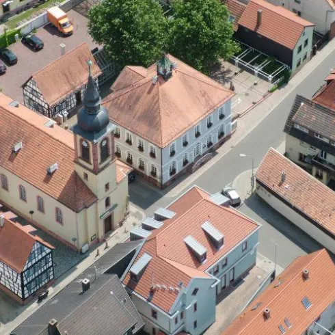 Eine malerische Stadtansicht mit rolfarbigen Dächern und einer Kirche. Die Straßen sind gut befahren und von Bäumen gesäumt.