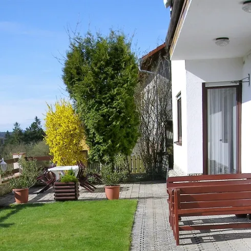 Ein schöner Garten mit grünem Rasen und bunten Pflanzen. Im Vordergrund stehen Sitzbänke und ein Wohnhaus im Hintergrund.