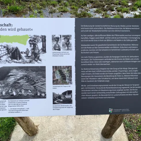 Ein Informationsschild über Landwirtschaft mit dem Titel „Mit Händen wird gebaut“. Es enthält Texte und Bilder, die landwirtschaftliche Praktiken und Geschichte darstellen.