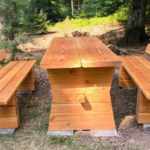 Ein Holzbank- und Tischset im Wald. Es bietet Platz für mehrere Personen und ist perfekt für ein Picknick in der Natur.