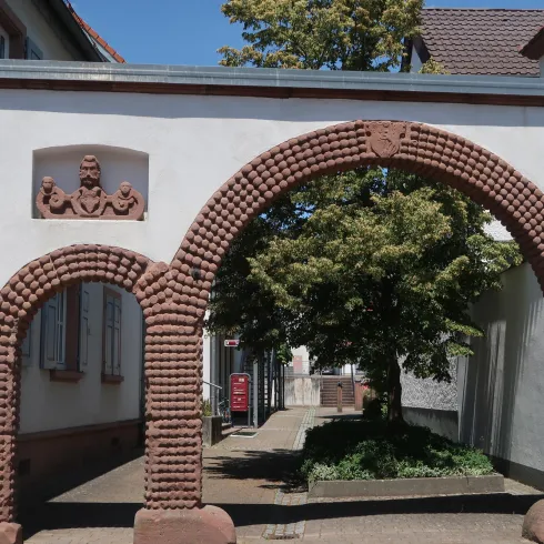 Ein historischer Torbogen mit dekorativen Steinen. Im Hintergrund ist ein grüner Baum sichtbar.