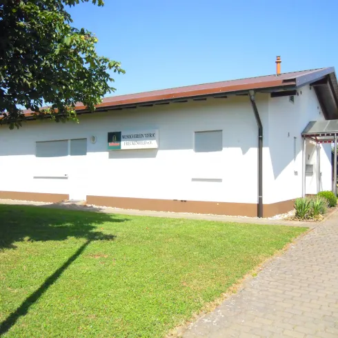 Ein modernes, weißes Gebäude mit einem leicht geneigten Dach. Der Eingangsbereich ist von einem gepflegten Garten umgeben.