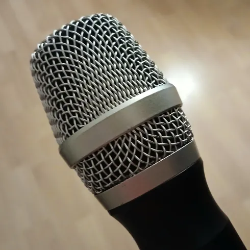 Ein nahes Bild eines Mikrofons mit einem silbernen Netz. Der Hintergrund ist aus Holz und unscharf.