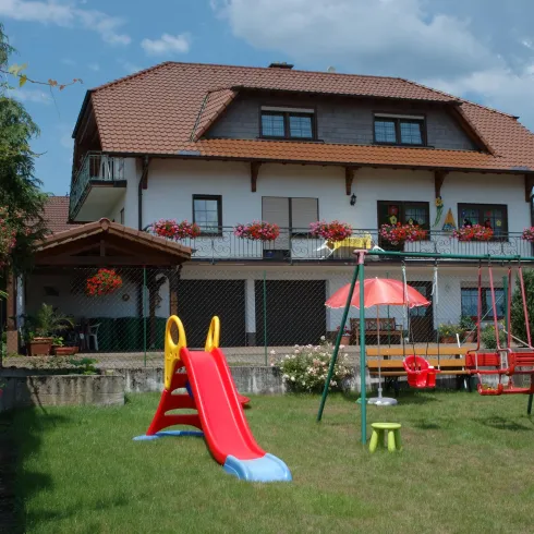 Ein schönes Haus mit einem gepflegten Garten. Im Garten befinden sich ein Klettergerüst und eine Rutsche für Kinder.