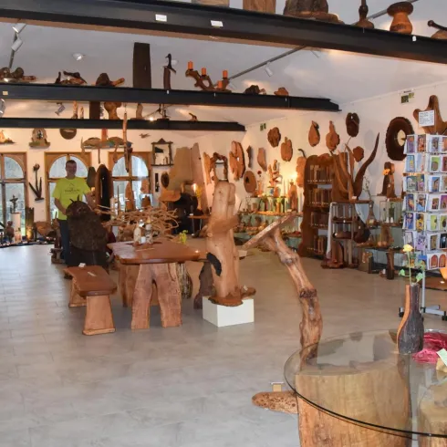 Ein gemütlicher Raum voller Holzskulpturen und Handwerkskunst. Die Wände sind mit kunstvollen Holzobjekten dekoriert, während Tische und Regale zum Stöbern einladen.