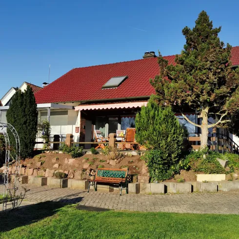 Ein modernes Haus mit rotem Dach und schöner Gartenanlage. Die Umgebung ist grün und einladend.