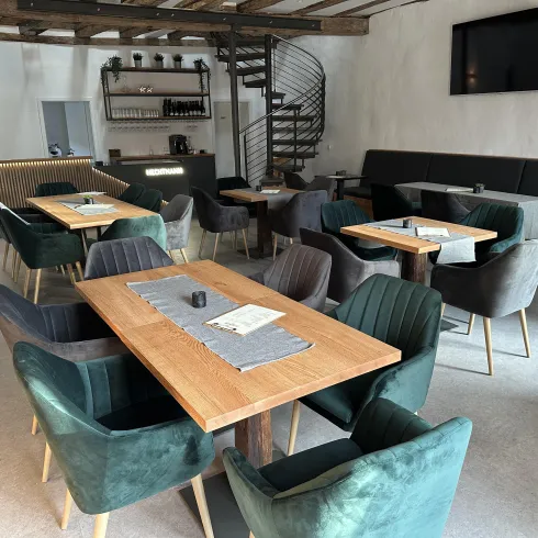 Ein modernes Restaurant mit stilvollen Tischen und Stühlen in Grün- und Grautönen. Die helle Innenausstattung vermittelt eine einladende Atmosphäre.