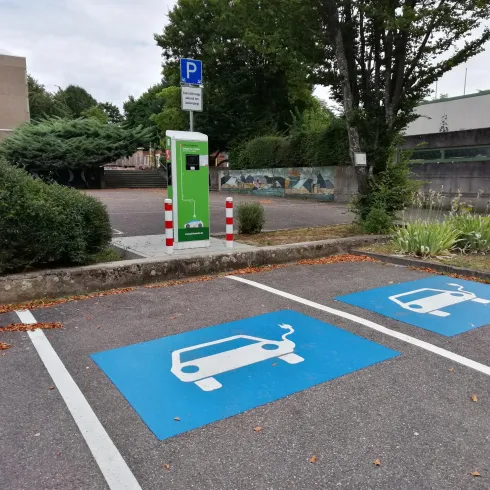 Zwei Parkplätze für Elektroautos mit Ladeanschlüssen sind klar markiert. Im Hintergrund steht eine Ladestation.