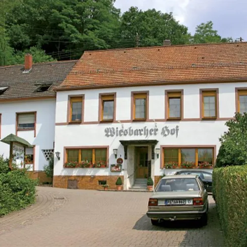 Ein traditionelles Gasthaus mit einem einladenden Eingang und großen Fenstern. Vor dem Haus steht ein Auto auf einem gepflasterten Weg.